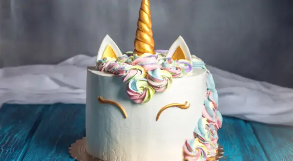En hemmagjord tårta med enhörningstema, perfekt för barnkalas. Med en gyllene horn, färgglad frosting och gulliga ögon.