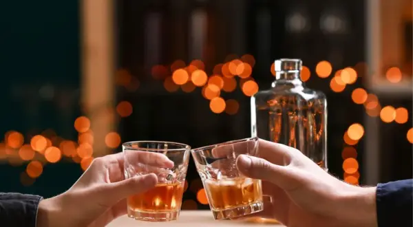 Dwie osoby wznoszą toast szklankami z bursztynowym płynem. Czysta wódka ma zero węglowodanów.