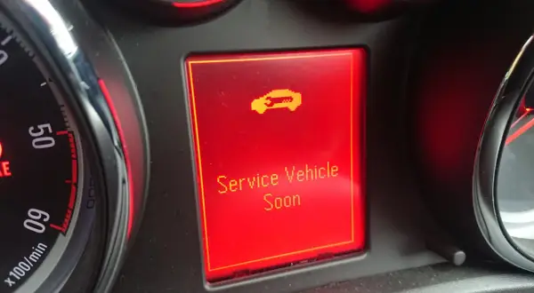 Wyświetlacz w Oplu Astrze H z komunikatem "Service Vehicle Soon" i ikoną samochodu.