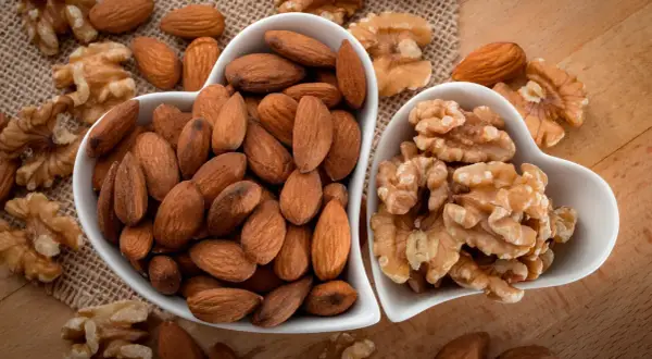 Deux bols en forme de cœur remplis d'amandes et de noix. Une belle présentation de ces oléagineux, parfaits pour une liste d'en-cas sains.
