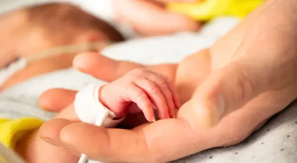Dłoń rodzica obejmuje maleńką dłoń dziecka z zespołem Edwardsa, otoczoną troską i nadzieją.
