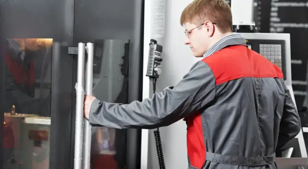 Ein Zerspanungsmechaniker öffnet die Tür einer CNC-Maschine. Er erkundet zerspanungsmechaniker weiterbildungsmöglichkeiten.
