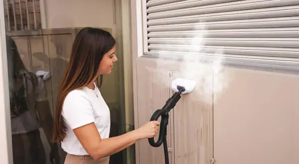 Donna pulisce le tapparelle con un pulitore a vapore, rimuovendo lo sporco in modo efficace.