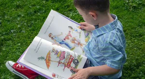 Chłopiec z zaciekawieniem czyta książkę z ilustracjami, która jest częścią bajkoterapii w przedszkolu.