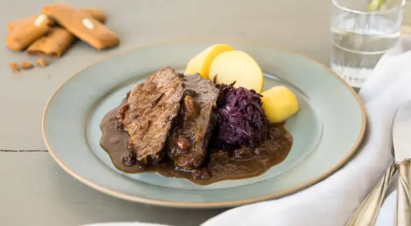 Ein Teller mit deftigem Braten, Rotkohl und Kartoffeln – ein schnelles Abendessen, das sättigt. Dazu ein Glas Wasser und ein paar Kekse.