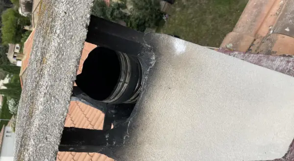 Détail d'un conduit de cheminée en métal noir, visiblement endommagé et encrassé, suggérant la nécessité de comment condamner un conduit de cheminée pour des raisons de sécurité.