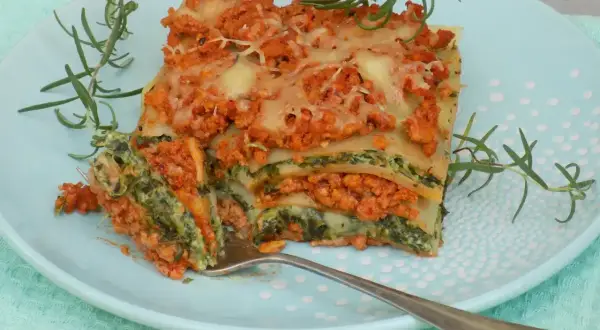 Pyszny przepis na lasagne z mięsem mielonym i szpinakiem, podana na talerzu z gałązkami rozmarynu.