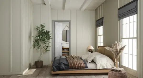 Letto in legno con coperte, posizionato di fianco alla porta aperta che conduce al bagno. Pianta in vaso e finestra con luce naturale.