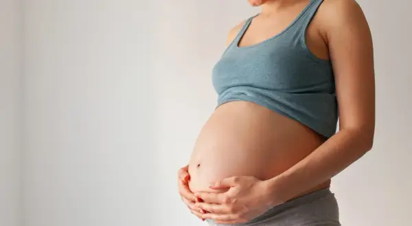 Uśmiechnięta ciężarna kobieta trzyma dłonie na brzuchu. Czas na poród, może już niedługo pojawi się czop śluzowy.