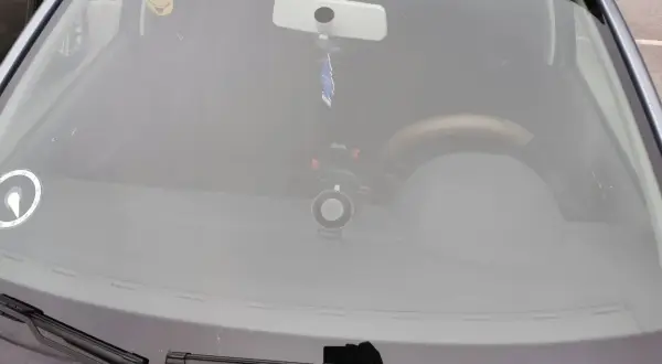 Bilens vindruta med en glad smiley-halsduk, backspegel och en dashcam. Perfekt för en stenskott besiktning.