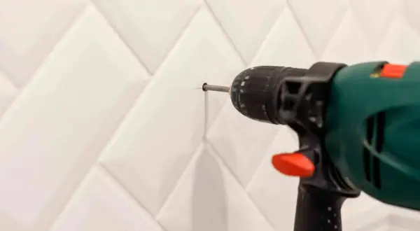Taladro perforando un agujero en una pared con azulejos blancos para colocar tacos.