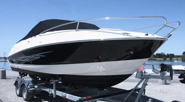 Barca sportiva bianca e nera su carrello, pronta per il varo. I candelieri sono i supporti metallici che la tengono ferma.