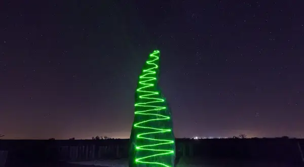 Menhir illuminato da una spirale di vernice elettroluminescente verde sotto un cielo stellato.