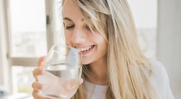 Une jeune femme souriante boit de l'eau osmosée dans un verre.