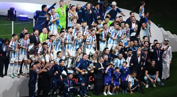 Piłkarze Argentyny świętują zwycięstwo, trzymając puchar. Wszyscy w biało-niebieskich strojach, z medalami na szyjach, tworzą najlepszą drużynę na świecie.