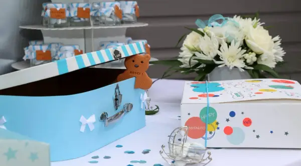 Décoration pour organiser un baptême : boîte à trésors bleue, ours en biscuit "Merci", fleurs blanches et boîtes cadeaux colorées.