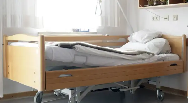Ein Pflegebett mit Holzrahmen und Rädern, bereit, wenn Sie ein Pflegebett beantragen müssen.