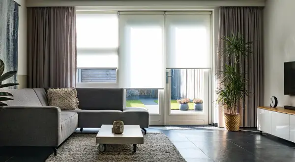 Nowoczesne zasłony do salonu inspiracje: szare, welurowe zasłony tworzą przytulną atmosferę, idealnie komponując się z szarą sofą i jasnymi roletami.