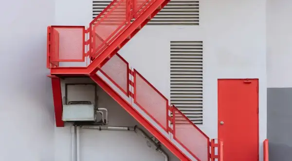 Czerwone, metalowe schody zewnętrzne prowadzą do czerwonych drzwi. Ciekawe, jakie schody do domu wybrać, by były tak efektowne!
