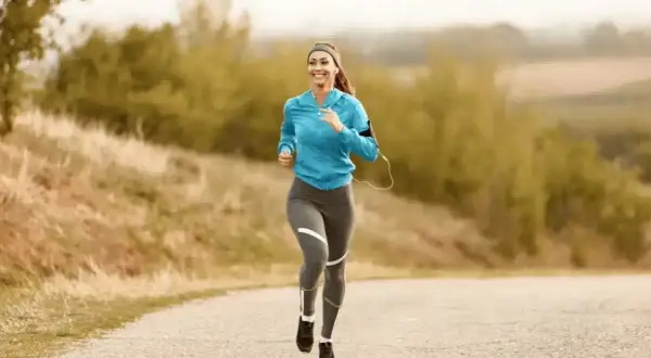Femme souriante courant sur une route de campagne, musique dans les oreilles, pour un sport à 180 bpm.