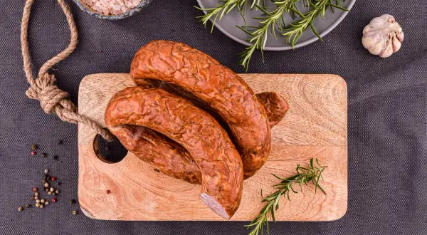Wędzona kiełbasa na desce z rozmarynem, solą i pieprzem.