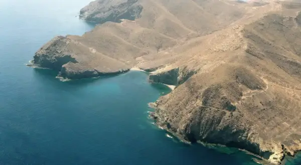 Vista aérea de la cala del bergantín, una bahía de aguas turquesas rodeada de montañas áridas y escarpadas.