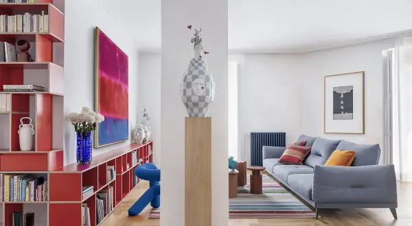 Estudios de arquitectura: sala de estar moderna con sofá azul, alfombra de rayas, estanterías rojas y arte abstracto.