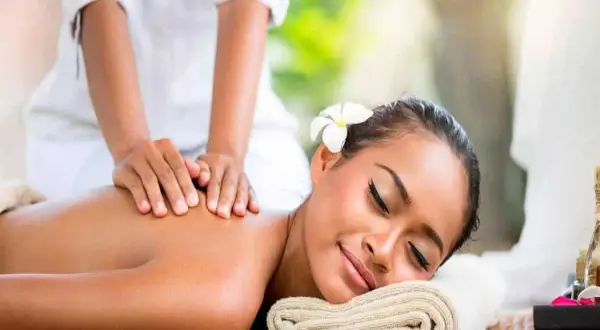 Mujer disfrutando un masaje relajante en un ritual spa. Una flor adorna su cabello mientras manos expertas alivian la tensión de su espalda.