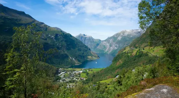 Widok na malownicze **Stavanger fiordy** z zielonymi zboczami gór, błękitną wodą i małym miasteczkiem u podnóża.
