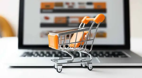 Miniaturowy wózek na zakupy przed ekranem laptopa symbolizuje najpopularniejsze sklepy internetowe i wygodne zakupy online.