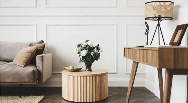Elegancki salon glamour z dominującym drewnem. Miękka sofa, okrągły stolik i stylowe biurko tworzą przytulną przestrzeń.