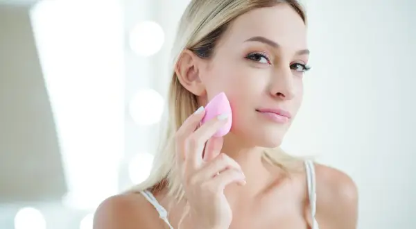 Blondynka z naturalnym pięknem, używa różowej gąbeczki do makijażu. Efekt make up no make up.
