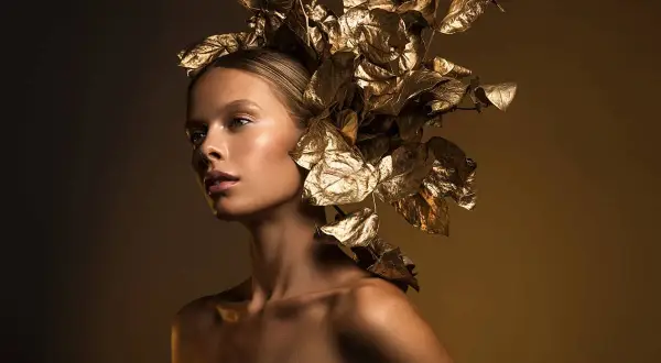 A model with a golden leaf headdress, captured with dramatic fashion lighting photography, showcasing a radiant glow.