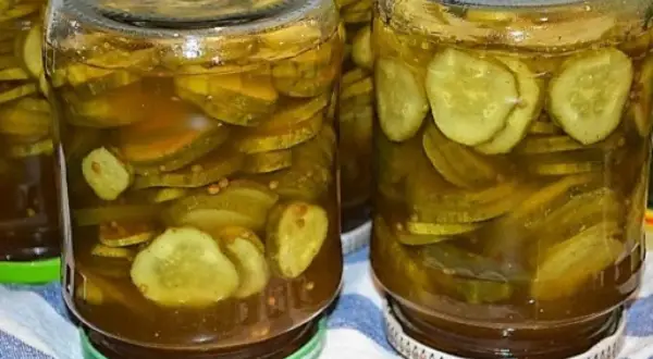 Słoiki pełne plasterków ogórków w zalewie z curry, ze skórką, gotowe do spożycia.