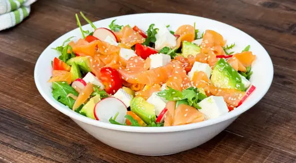 Insalata fresca con salmone affumicato, avocado, pomodorini, ravanelli e cubetti di formaggio, cosparsa di semi di sesamo.