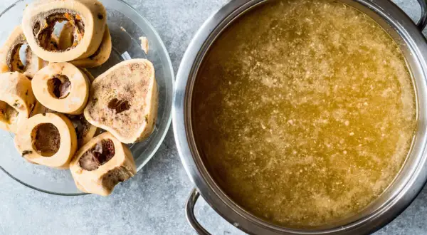 Un plato con huesos de tuétano y una olla con caldo dorado, perfecto para preparar caldo de huesos para perros.