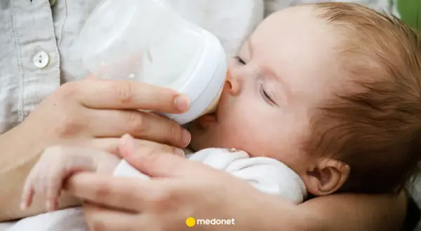 Dziecko pije mleko modyfikowane z butelki. Mama karmi maluszka, który spokojnie zasypia.