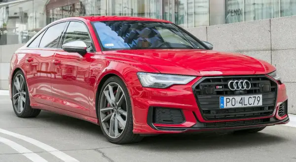 Czerwone Audi S6 C8 z polskimi tablicami rejestracyjnymi, zaparkowane przed nowoczesnym budynkiem z lustrzaną fasadą.