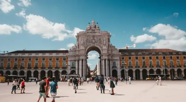 En solig dag på ett stort torg i Lissabon, Portugal. Människor promenerar under en imponerande triumfbåge. Ett perfekt restips för Portugal.