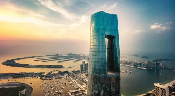 Imponujący, szklany wieżowiec, najwyższy hotel na świecie, góruje nad Dubajem o zachodzie słońca. Widok na sztuczne wyspy w kształcie palmy.