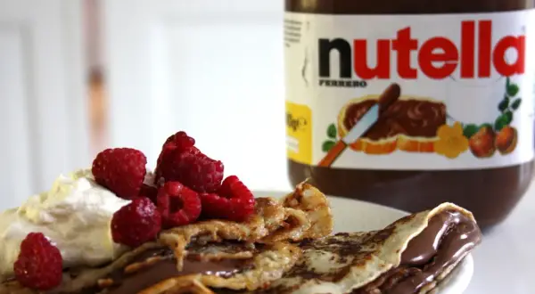 En pannkakstårta med nutella, grädde och hallon. En burk nutella syns i bakgrunden.