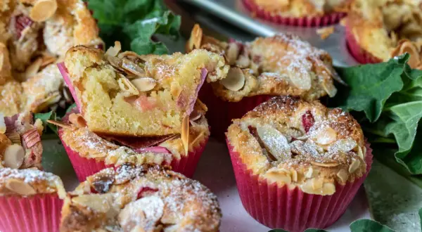 Fluffiga rabarber muffins med mandelflagor och pudersocker, bakade i rosa muffinsformar.