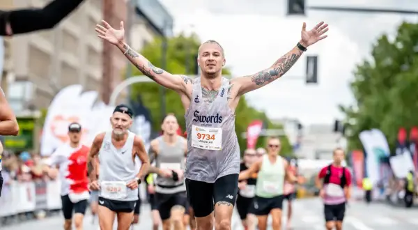 Triumfujący biegacz z tatuażami, z rękami w górze, na maratonie poniżej 2h.