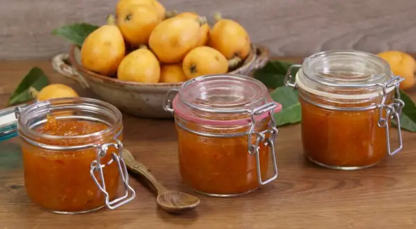 Tre barattoli di marmellata di nespole fatti in casa, con nespole fresche in una ciotola sullo sfondo.