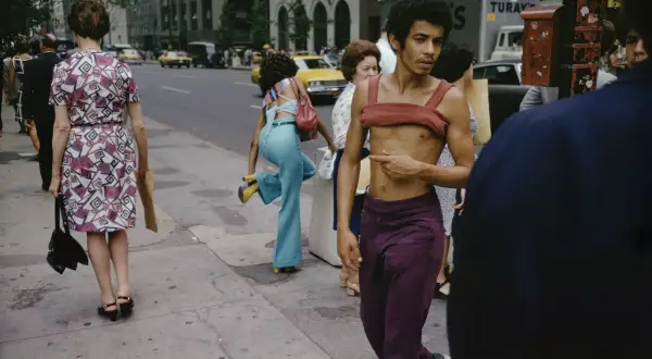 Ulica Nowego Jorku uchwycona przez Joel Meyerowitz. Mężczyzna w bordowym topie i fioletowych spodniach, obok kobiety w kwiecistej sukience.