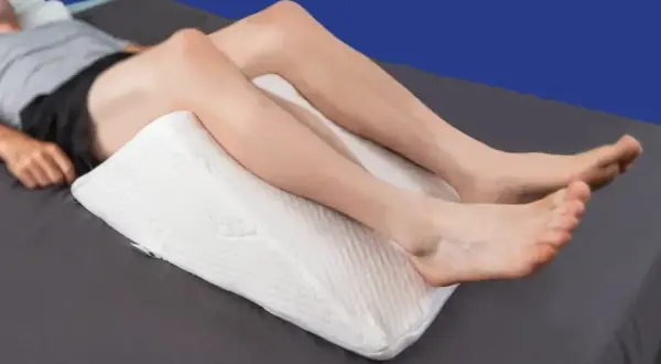 A person is resting with a white wedge pillow under their knees, providing comfort for sleeping with pillow under knees.
