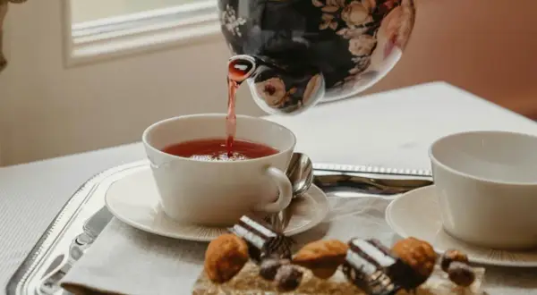 Tetera floral vierte té rojo en taza blanca. Bandeja con dulces y otra taza, perfecto para la hora del té en Inglaterra.