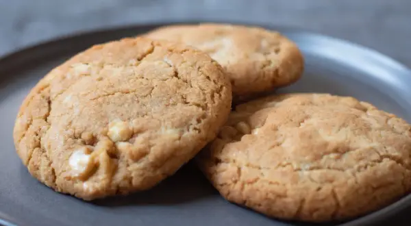 Tre gyllene white chocolate chip cookies på en mörkgrå tallrik, redo att avnjutas.