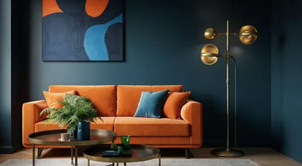 Ein orangefarbenes Sofa und ein abstraktes Gemälde schaffen ein warmes Wohnzimmer. Ein Messing-Stehleuchte sorgt für gemütliches Licht.