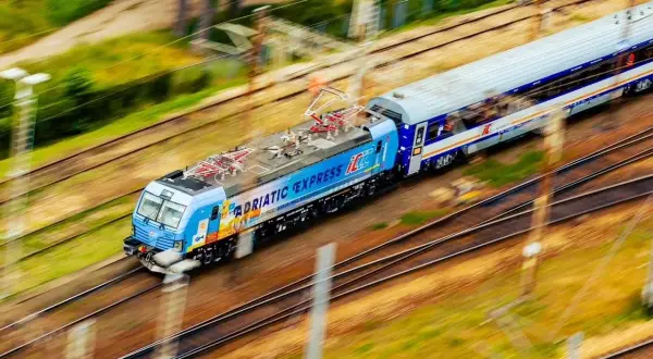Pędzący pociąg "Adriatic Express" na trasie z Warszawy do Łodzi, z rozmytym tłem zieleni i torów.